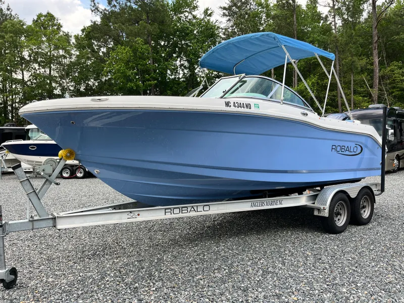 Slide: The Image of 2024 Robalo R207 Dual Console boat on trailer, blue hull, parked outdoors. - 5