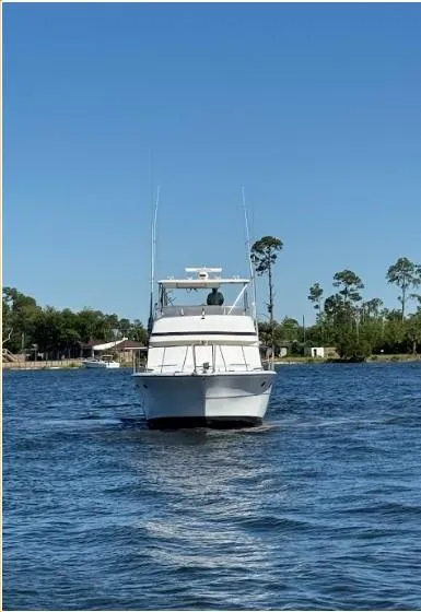 Slide: The Image of 1989 Ricker 48 Convertible yacht cruising on a calm lake under a clear blue sky. - 23