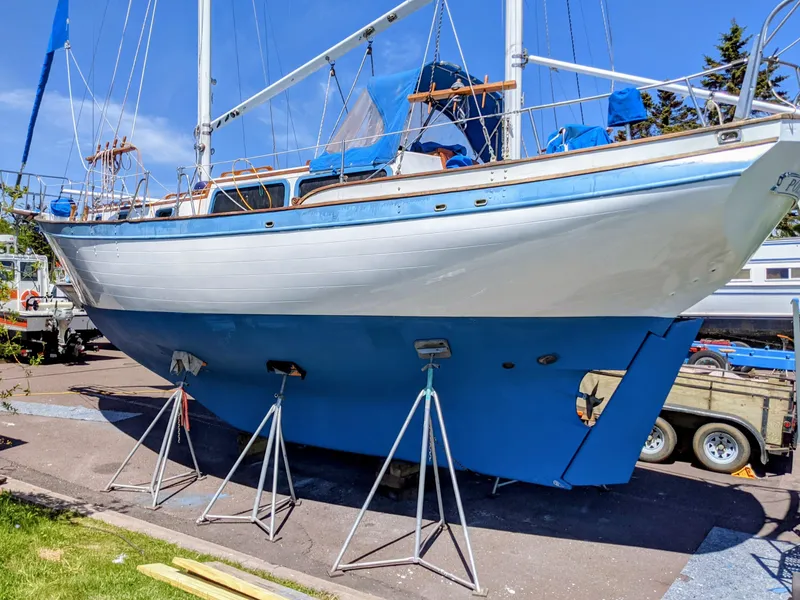 Slide: The Image of 1975 Downeast Ketch sailboat on stands, blue and white hull, sunny day. - 2