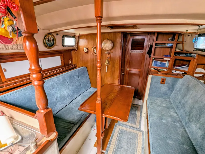 Slide: The Image of 1975 Downeast Ketch interior with wooden furnishings and blue seating. - 24
