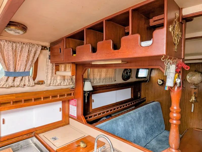 Slide: The Image of 1975 Downeast Ketch interior with wooden cabinetry, blue seating, and nautical decor. - 26