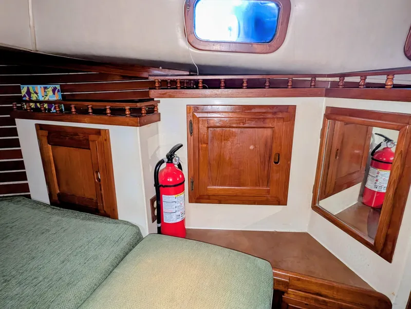 Slide: The Image of 1975 Downeast Ketch interior with wooden cabinets, fire extinguisher, and cushioned seating. - 39