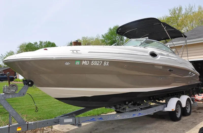 Slide: The Image of 2006 Sea Ray 240 Sundeck boat on trailer, parked outdoors with trees in background. - 2