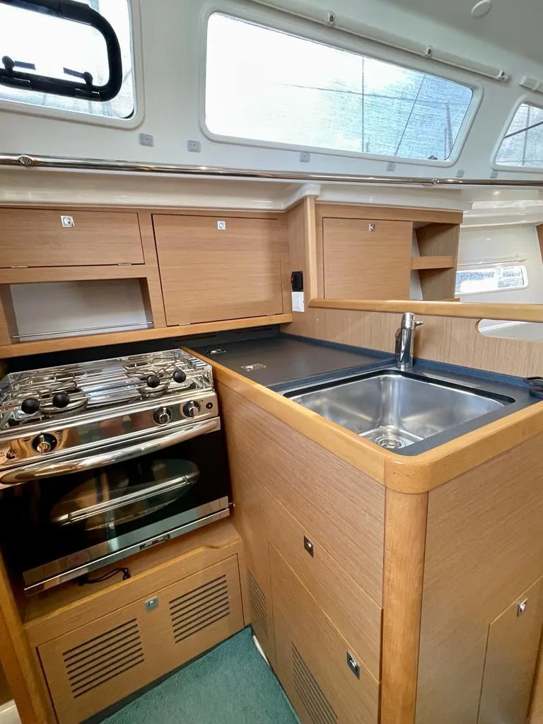 Slide: The Image of 2021 Jeanneau Sun Odyssey 319 yacht kitchen with stove, sink, and wooden cabinetry. - 9