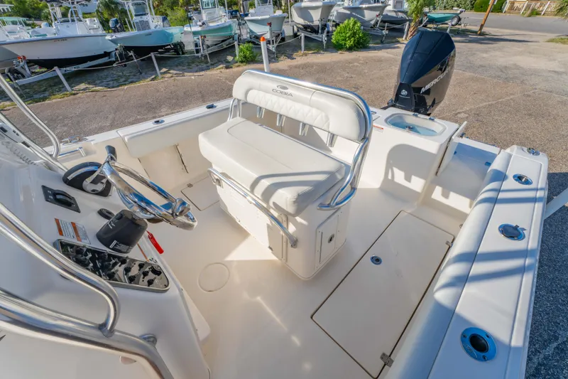 Slide: The Image of 2022 Cobia 237 CC boat interior with seating and steering wheel, parked outdoors. - 19