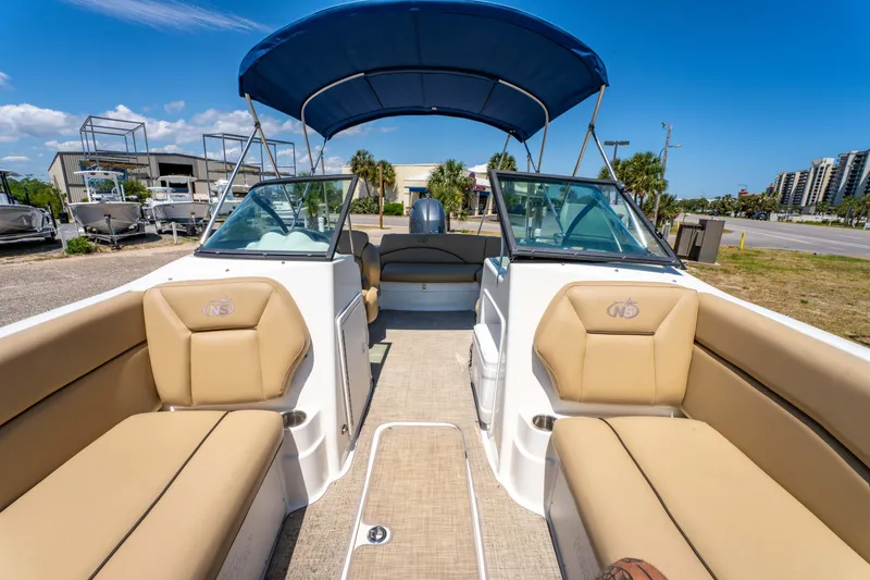 Slide: The Image of 2020 NauticStar 203 DC boat with tan seating and blue canopy, docked under clear skies. - 18