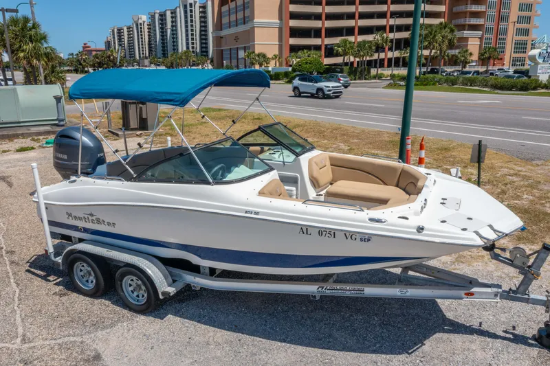 Slide: The Image of 2020 NauticStar 203 DC boat on trailer with blue canopy, parked near road. - 2