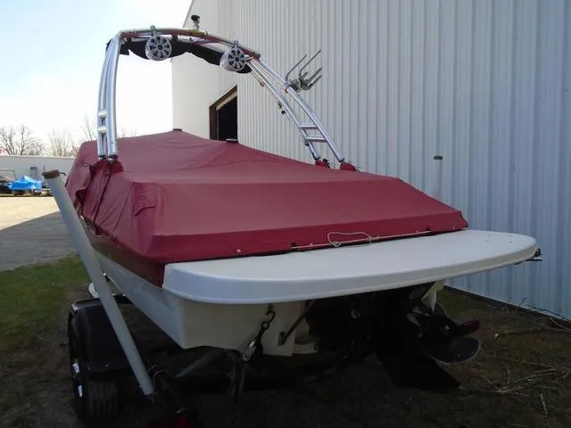Slide: The Image of 2013 Bayliner 185 Bowrider with red cover, parked near a building. - 18