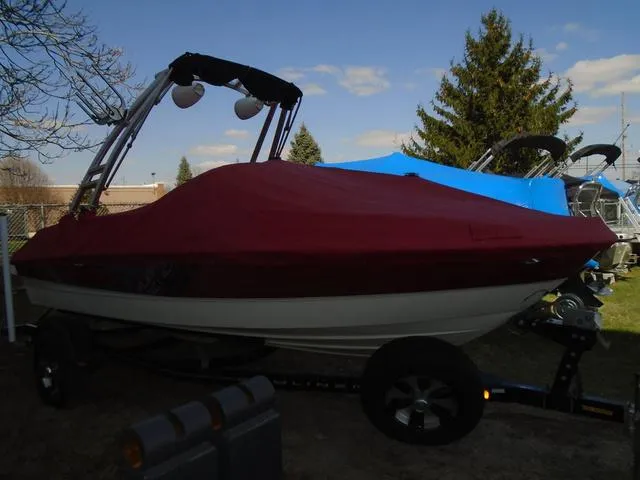 Slide: The Image of 2013 Bayliner 185 Bowrider with red cover on trailer, parked outdoors. - 19