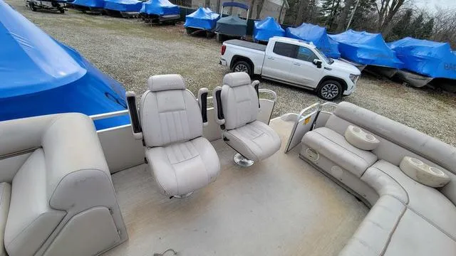 Slide: The Image of 2000 Godfrey Pontoons San Pan interior with beige seating, parked near covered boats and a white truck. - 7