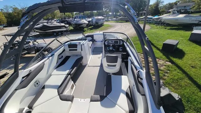 Slide: The Image of 2022 Yamaha Boats AR210 interior with sleek seating and modern dashboard, parked outdoors. - 2