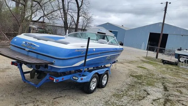Slide: The Image of 2004 MasterCraft MariStar 210 boat on trailer, parked outdoors near a large blue building. - 7