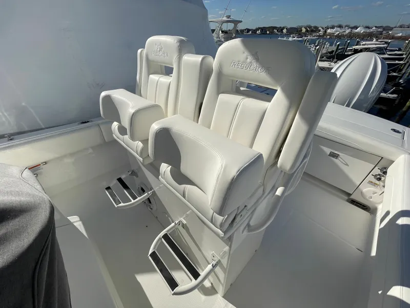 Slide: The Image of 2022 Regulator 28 boat with white cushioned seats and footrests, docked at a marina. - 17