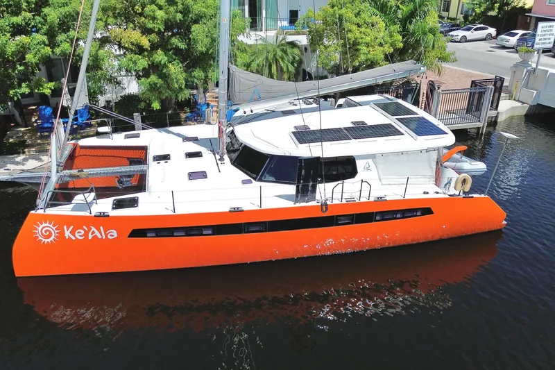 Slide: The Image of Orange and white Balance 482 catamaran docked, featuring solar panels and lush greenery in the background. - 158