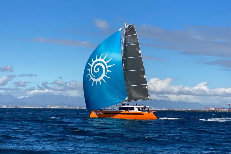 Slide: The Image of Orange Balance 482 catamaran sailing with blue sail, ocean and cityscape background. - 175