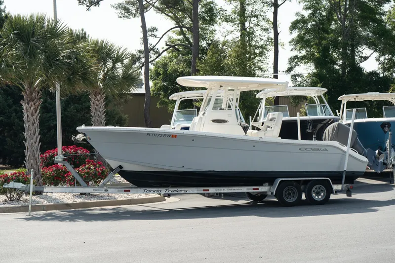 Slide: The Image of 2019 Cobia 240 Center Console boat on trailer, parked near palm trees and flowers. - 11