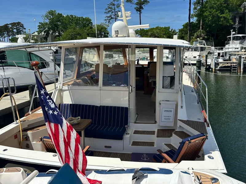 Slide: The Image of 2004 Grand Banks 49 Eastbay HX yacht docked, featuring a spacious deck and American flag. - 1