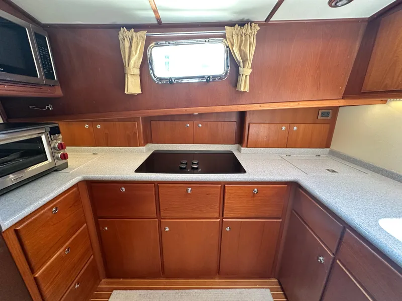 Slide: The Image of 2004 Grand Banks 49 Eastbay HX galley with wooden cabinetry, stovetop, and window. - 52