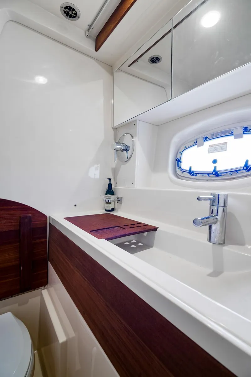 Slide: The Image of 2013 Sea Ray 410 Sundancer bathroom with modern sink, mirror, and porthole window. - 24