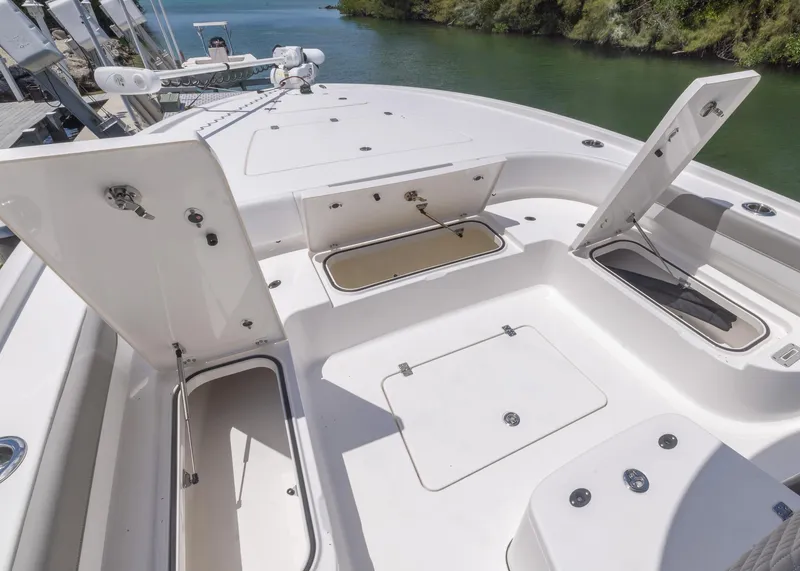 Slide: The Image of 2023 Caymas 28 HB boat deck with open storage compartments, docked by lush greenery. - 12