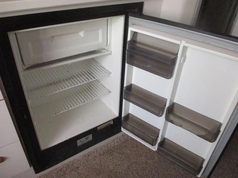 Slide: The Image of Empty refrigerator inside a 1991 Sea Ray 350 Express Cruiser, featuring wire shelves and door compartments. - 23