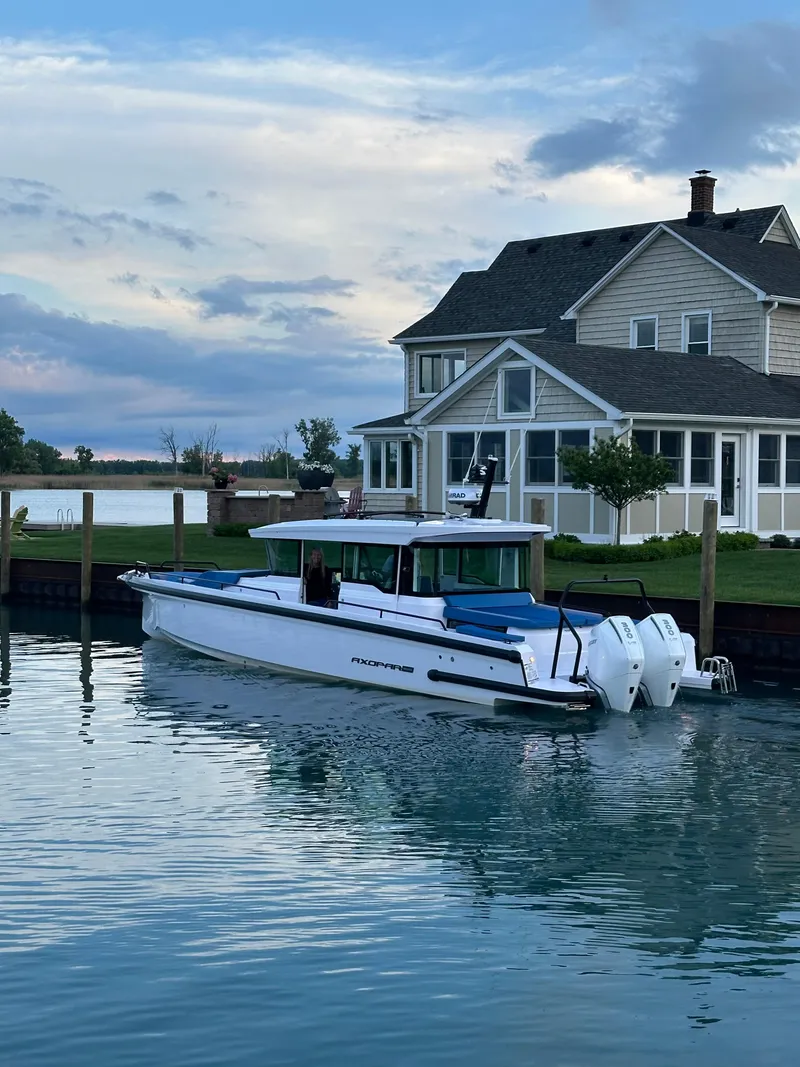 Slide: The Image of 2024 Axopar 37 XC Cross Cabin Aft Cabin boat docked near a waterfront house. - 2