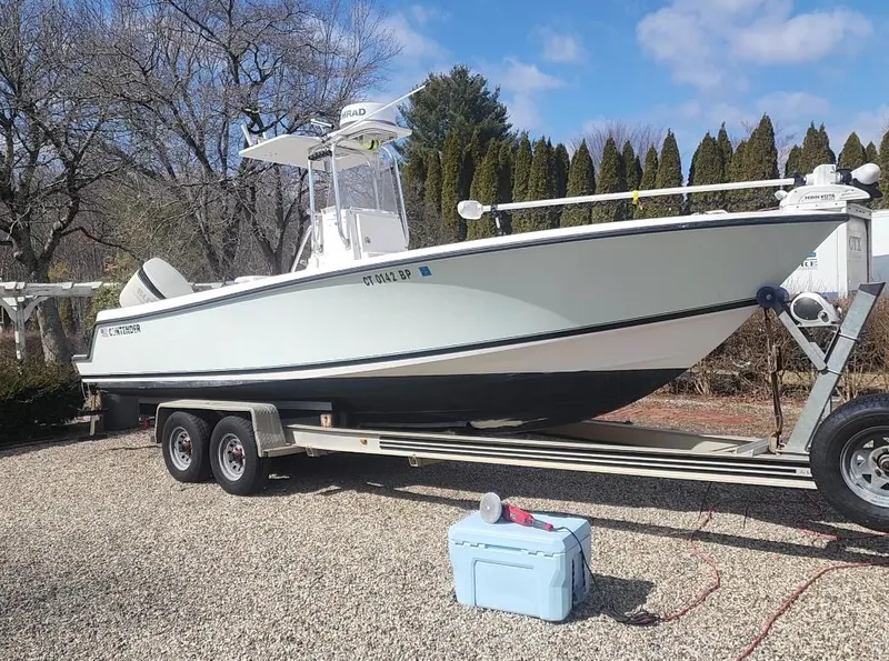 The Image of 2005 Contender 23 Tournament boat on trailer, parked on gravel with trees in background. - 0