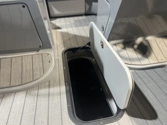 Slide: The Image of 2024 Manitou LX 23 RFXW boat storage compartment with open hatch on textured flooring. - 11