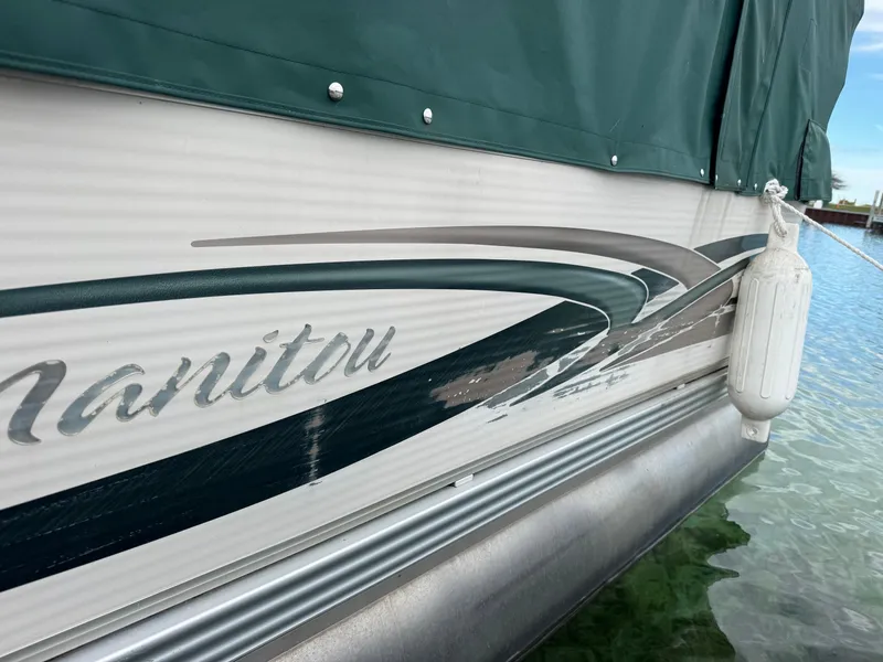 Slide: The Image of 2007 Manitou Legacy boat side view with green cover and water reflection. - 15