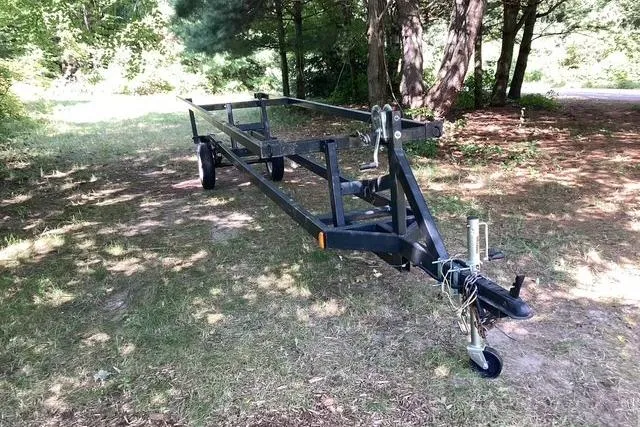 Slide: The Image of 2007 Manitou Legacy trailer in a wooded area, showcasing sturdy metal frame and hitch. - 18