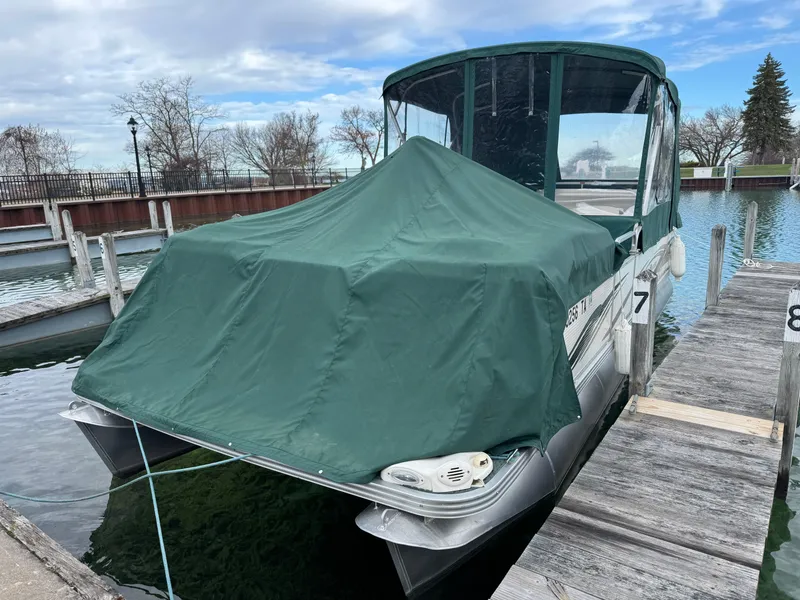 Slide: The Image of 2007 Manitou Legacy boat docked with green cover, under a partly cloudy sky. - 5