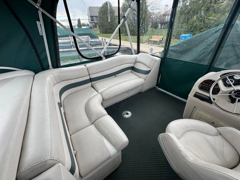 Slide: The Image of 2007 Manitou Legacy boat interior with white seating and steering wheel, docked near greenery. - 8