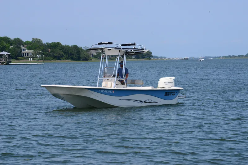 Slide: The Image of 2018 Carolina Skiff 218 DLV boat cruising on a calm lake with a scenic shoreline. - 4