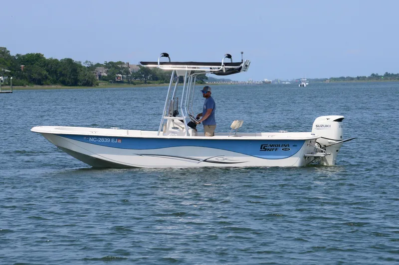 Slide: The Image of 2018 Carolina Skiff 218 DLV boat on water with person steering, scenic background. - 5