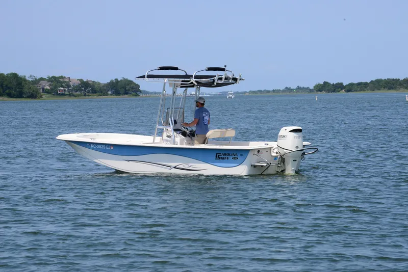 Slide: The Image of 2018 Carolina Skiff 218 DLV boat on calm water with a person at the helm. - 6
