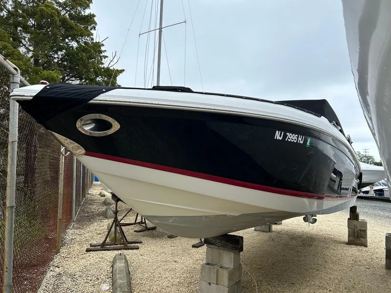 The Image of 2010 Cobalt 262 boat on blocks, black hull with red stripe, parked outdoors. - 0