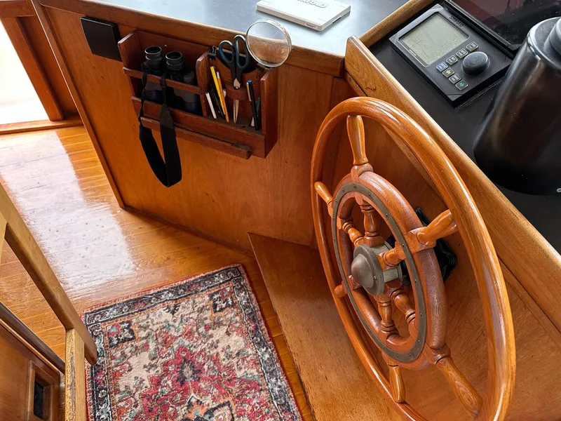 Slide: The Image of 1989 Pilgrim Trawler helm with wooden wheel, navigation tools, and a decorative rug. - 17