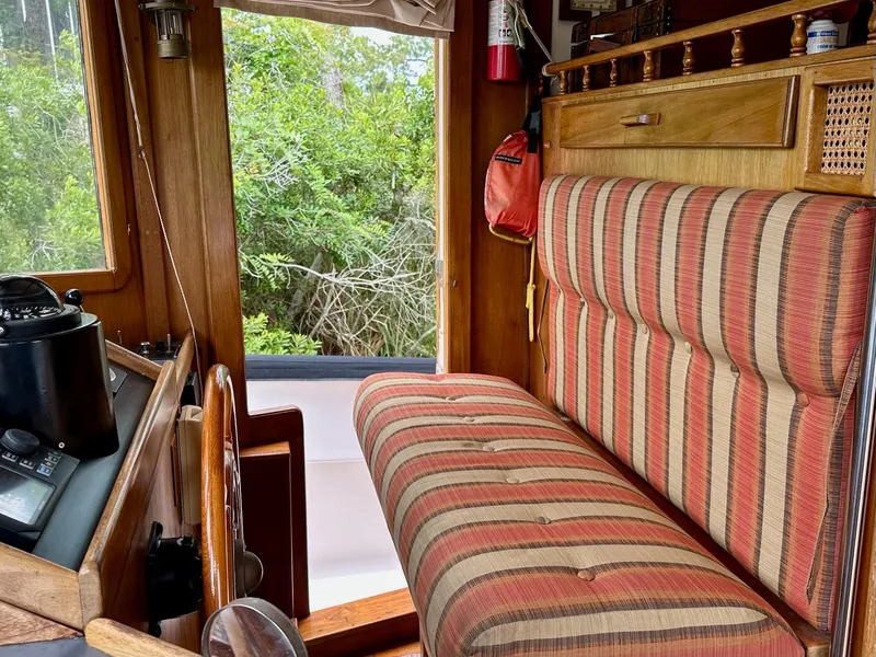 Slide: The Image of 1989 Pilgrim Trawler interior with striped seating, wooden accents, and lush greenery outside. - 18