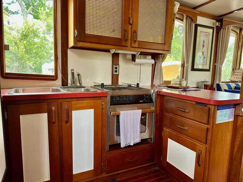 Slide: The Image of 1989 Pilgrim Trawler kitchen with wooden cabinets, stove, and red countertops. - 23