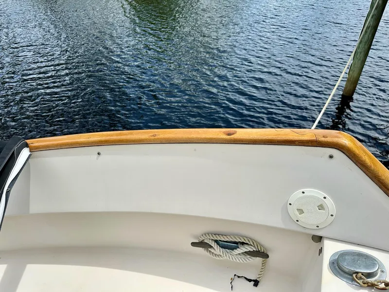 Slide: The Image of 1989 Pilgrim Trawler boat deck with wooden railing and rope, docked on calm water. - 43