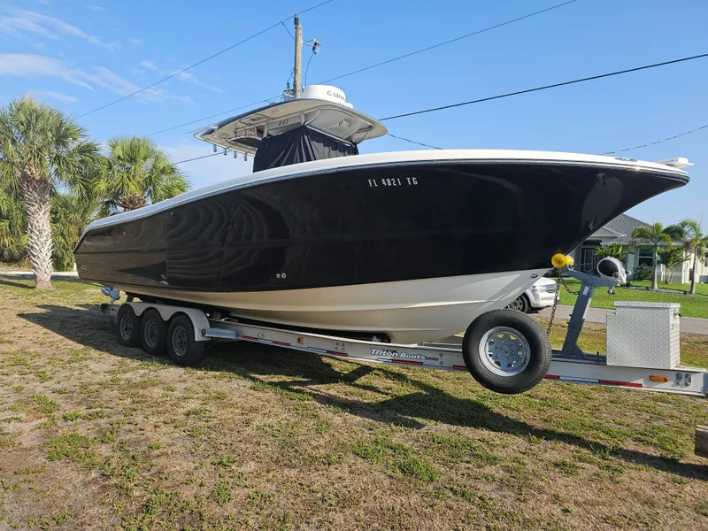 Slide: The Image of 2010 Triton 301 CC boat on trailer, parked outdoors with palm trees in background. - 2