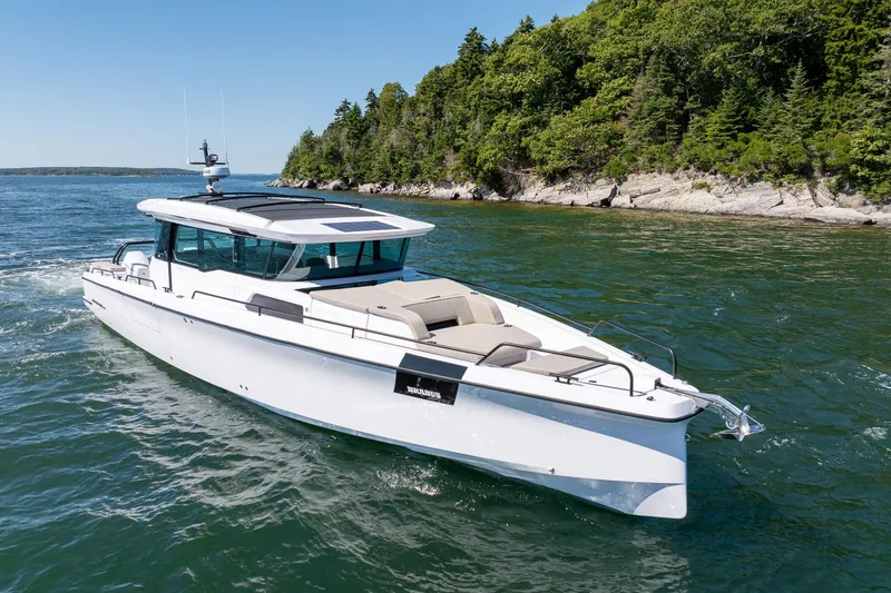 Slide: The Image of 2025 Axopar 45 boat cruising near a forested shoreline. - 2