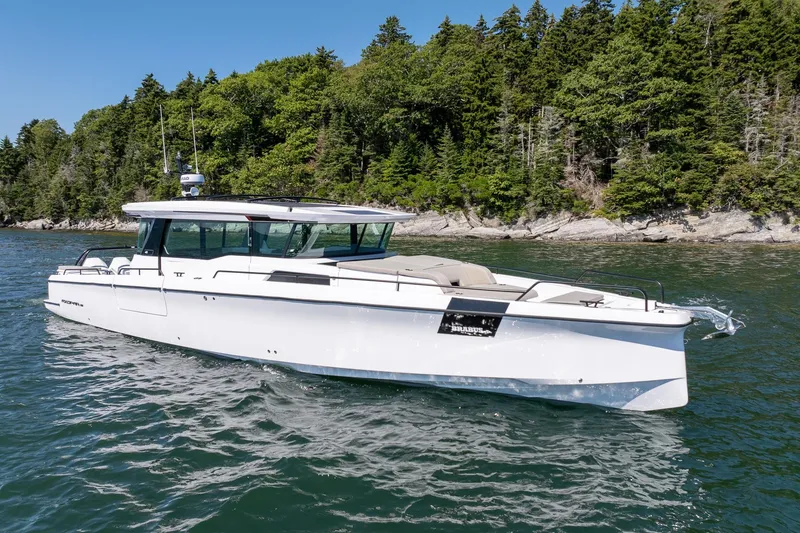 Slide: The Image of 2025 Axopar 45 boat with open storage compartment, scenic forested shoreline in background. - 29