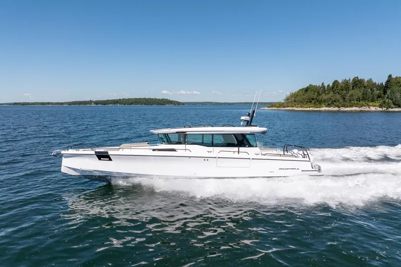 Slide: The Image of 2025 Axopar 45 boat cruising on a sunny day near a forested shoreline. - 8
