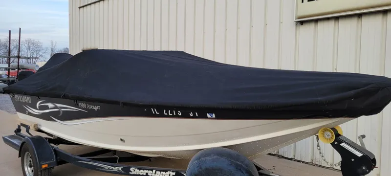 Slide: The Image of 2004 Sylvan F 1800 Avenger boat with cover on trailer, parked by a building. - 26