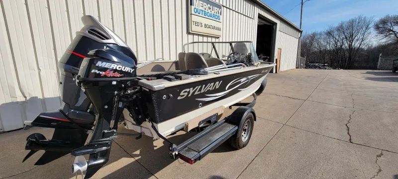 Slide: The Image of 2004 Sylvan F 1800 Avenger boat with Mercury outboard motor on trailer, parked outside a building. - 4