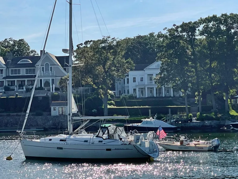 Slide: The Image of Sailboat Beneteau 361 (1999) anchored near waterfront homes, with American flag, under clear sky. - 2