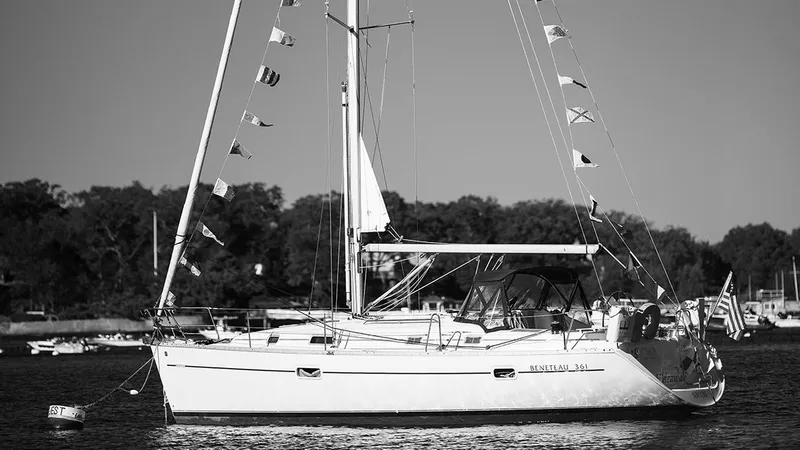 Slide: The Image of 1999 Beneteau 361 sailboat on calm water, adorned with flags, trees in background. - 3