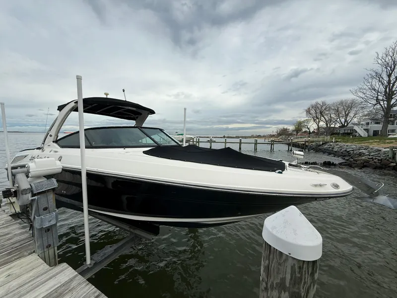 Slide: The Image of 2010 Sea Ray 300 SLX boat docked on a lift by the water, under cloudy skies. - 2