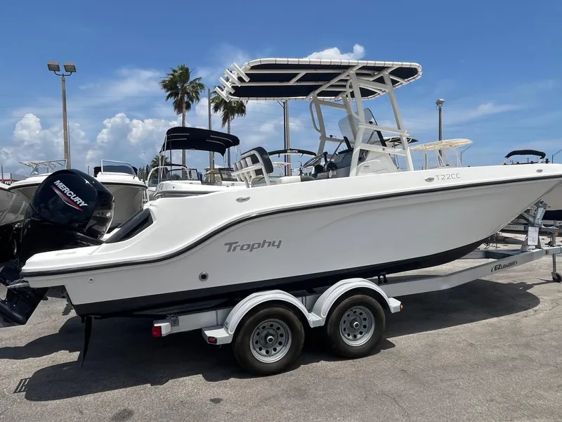 Slide: The Image of 2022 Bayliner Trophy T22CC boat on trailer, parked outdoors under clear sky. - 1